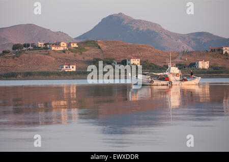 Greek traditional wooden fishing boat and captain on stern post during fishing time at Diapori beach/ Kontias bay early morning Stock Photo