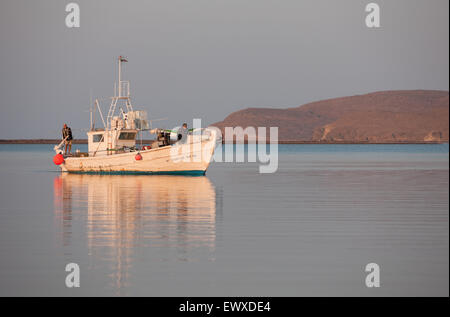 Greek traditional wooden fishing boat and captain on stern post manouevring at Diapori beach/ Kontias bay early morning. Lemnos Stock Photo