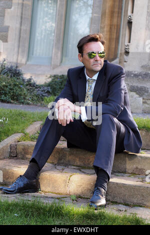 Smart middle-aged man sitting in a aprk wearing a business suit and sunglasses Stock Photo