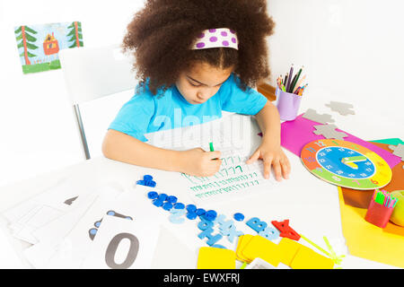 Concentrated African girl writes letters at table Stock Photo