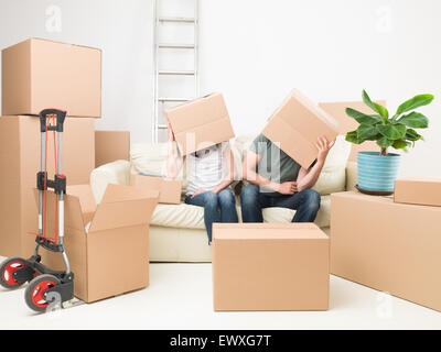 couple sitting on sofa with boxes on their heads, in new house Stock Photo