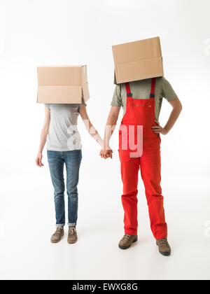 young couple with cardboard boxes on their heads, holding hands, on white background Stock Photo