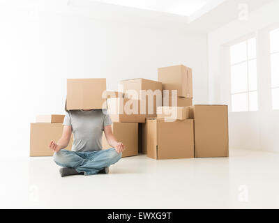 man sitting on floor in new apartment, meditating with box on his head Stock Photo