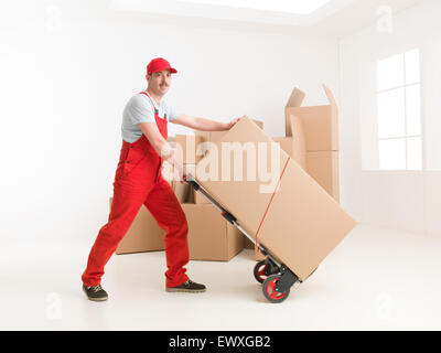 full length of young caucasian deliveryman with hand truck, transporting cardboard boxes. moving house Stock Photo