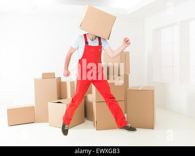 overjoyed delivery man jumping in warehouse with box covering his head Stock Photo