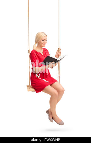 Vertical shot of a young woman in a red dress sitting on a swing and reading a book isolated on white background Stock Photo