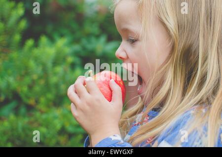 Side view of a girl about to take a bite out of an apple Stock Photo