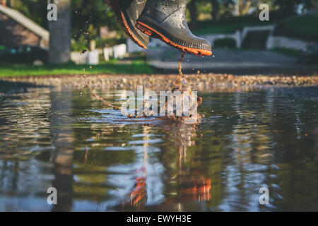 Low angle close-up of a boy jumping in a muddy puddle Stock Photo