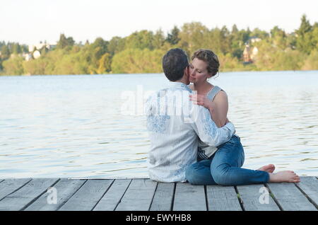 Couple sitting on a wooden jetty embracing Stock Photo