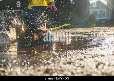 Boy jumping in puddle of muddy water Stock Photo