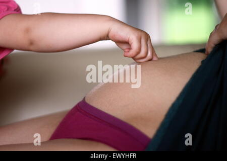 Baby hand touching the belly of her pregnant mother Stock Photo