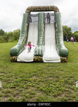 Young girl on bouncy castle slide while another girl is about to go down.at the Canada Day festivities in Cannington Ontario Stock Photo