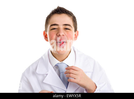 Boy dressed as a doctor in light blue tie and white coat helps to feel medicine more friendly: he is showing his tongue with a pill on it. His acne skin has not ben retouched Stock Photo