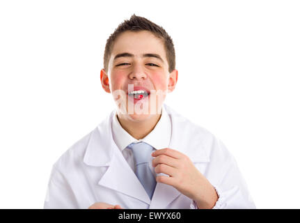 Boy dressed as a doctor in light blue tie and white coat helps to feel medicine more friendly: he is showing his tongue with a pill on it. His acne skin has not ben retouched Stock Photo