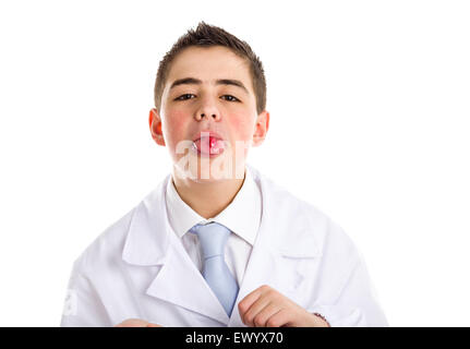 Boy dressed as a doctor in light blue tie and white coat helps to feel medicine more friendly: he is showing his tongue with a pill on it. His acne skin has not ben retouched Stock Photo