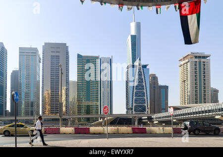 Businessman in Dubai walking under the UAE flag in front of the Jumeirah Lake Towers Stock Photo