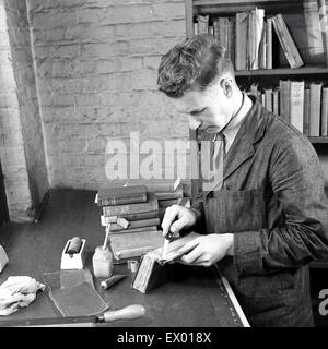 Historical, 1950s, picture shows a male bookbinder working at his bench gluing the spine onto a book. Stock Photo