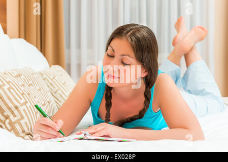beautiful brunette woman taking notes in a notebook lying on the bed Stock Photo