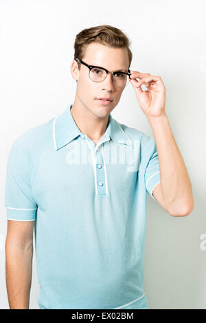 A handsome young man wearing 50s eye glasses and vintage top, posing with and looking away Stock Photo