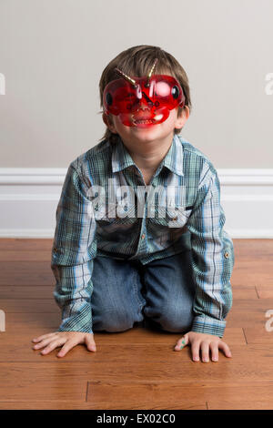 Portrait of young boy, kneeling on floor, wearing mask Stock Photo