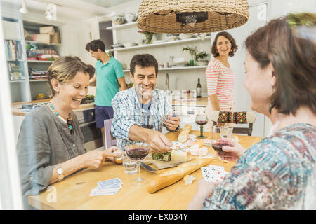 Five adult friends playing cards at dining table Stock Photo