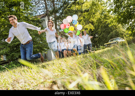 Group of people running through forest, boy holding bunch of balloons Stock Photo