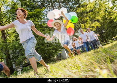 Group of people running through forest, boy holding bunch of balloons Stock Photo