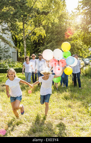 Group of people running and walking through forest, boy holding bunch of balloons Stock Photo