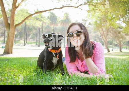 Portrait of young woman and dog lying in park wearing sunglasses Stock Photo