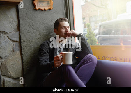 Young man sitting in cafe window seat looking out of window Stock Photo