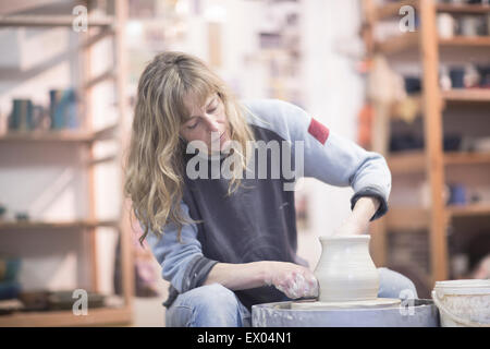Female potter forming clay pot on pottery wheel in workshop Stock Photo