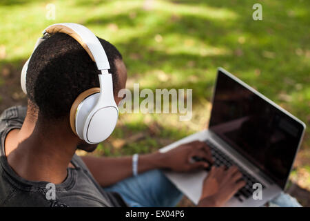 Young man, outdoors, wearing headphones and using laptop, rear view Stock Photo