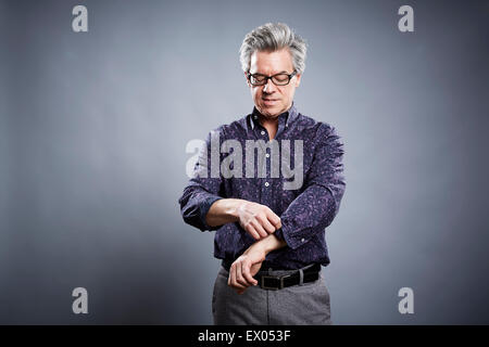 Studio portrait of mature businessman rolling up his sleeves Stock Photo