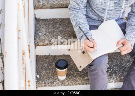 Man sitting on steps writing in notebook Stock Photo