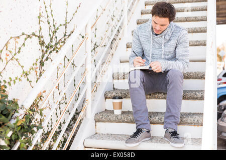 Young man sitting on steps writing Stock Photo