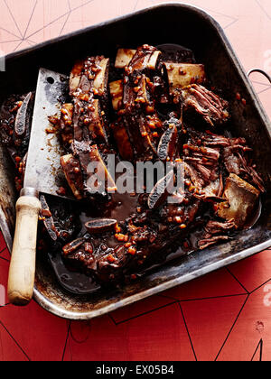 Roasting tin of short ribs braised in black sauce with butchers knife Stock Photo