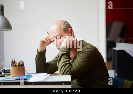Mature man at desk leaning on elbow Stock Photo