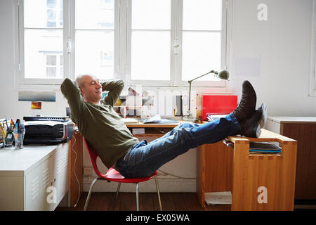 Mature man sitting with feet up at desk Stock Photo