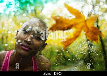Portrait of young woman looking through rain covered window Stock Photo