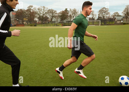 Two male soccer players running with ball on soccer pitch Stock Photo