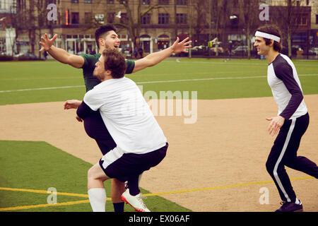 Three male soccer players celebrating on soccer pitch Stock Photo