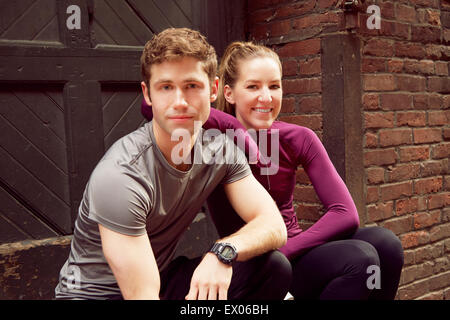 Portrait of young male and female runners sitting on alley step Stock Photo