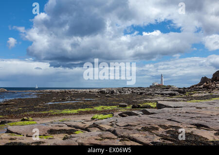 A yacht heads towards the lighthouse on St Mary's Island, viewed from Collywell Bay at low tide, Seaton Sluice, England, UK Stock Photo