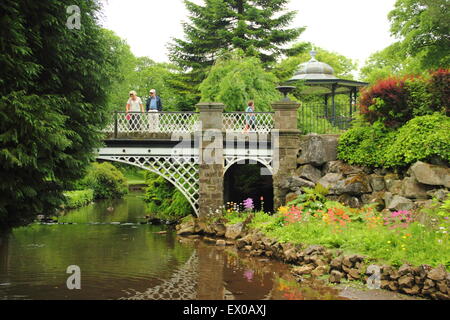 A man and woman pause on a bridge near the bandstand (pictured) in the Pavilion Gardens in Buxton Derbyshire England - summer 20 Stock Photo