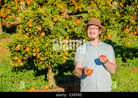 Cheerful young man juggling oranges on citrus farm Stock Photo