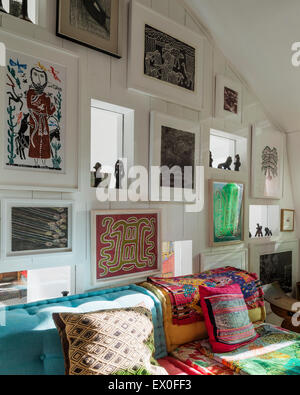 Assorted art on wall including work by J Borges and J Pike above blue buttoned sofa with Guatemalan textiles Stock Photo