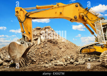 Yellow excavator and a heap of dirt, in the background a nice blue sky with white clouds Stock Photo