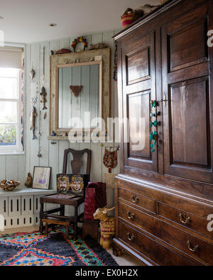 Antique wardrobe and chair in room corner with wooden mirror adorned with small ojects from all over the world Stock Photo