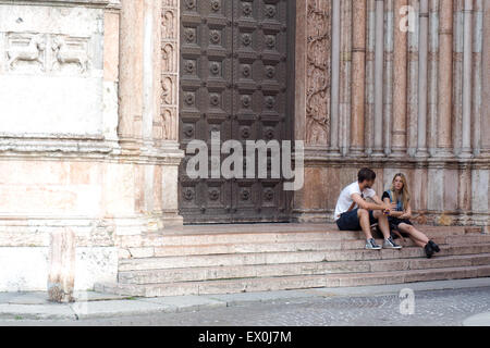 A young couple sitting on the steps to the entrance of the Baptistery of Parma Cathedral, Stock Photo