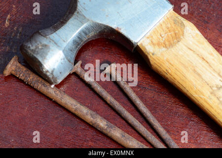 Three old nails and a hammer on top a wooden workshop table Stock Photo